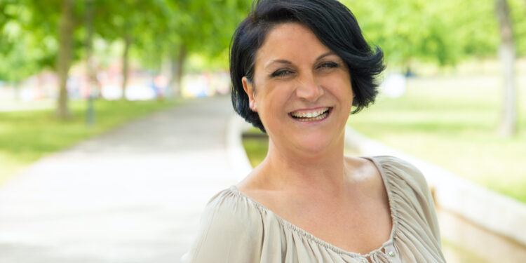 Cheerful excited woman walking in park and laughing. Mature black haired lady enjoying nature outdoors and smiling at camera. Happy woman outdoors concept