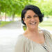 Cheerful excited woman walking in park and laughing. Mature black haired lady enjoying nature outdoors and smiling at camera. Happy woman outdoors concept